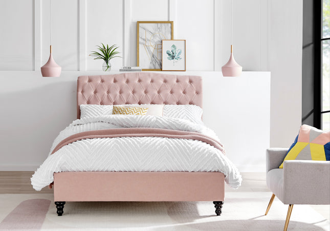 A pink upholstered double bed with a button headboard, wooden feet, 