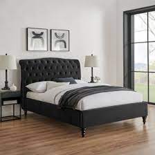A black upholstered double or king-size bed with a button style headboard, wooden feet, and a white mattress,